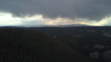 Aerial-View-of-Storm-Clouds-Looming-in-the-Distance-in-the-Forested-Mountains-of-Colorado,-Tilt-Down,-Backwards-Motion