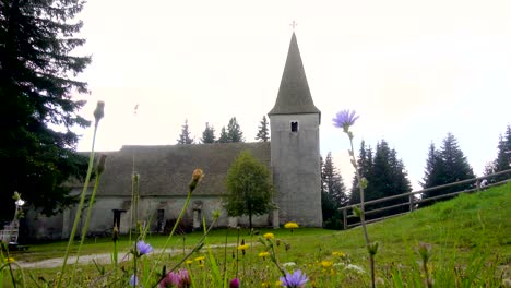 Time-lapse,-dramatic-clouds-above-alpine-church-and-meadow-with-flowers-in-front,-Trije-Kralji,-Pohorje,-Slovenia