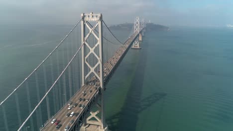 Luftaufnahme-Von-Fahrzeugen,-Die-Sich-Auf-Der-San-Francisco-oakland-Bay-Bridge-Mit-Der-Stadt-Im-Hintergrund-Bewegen