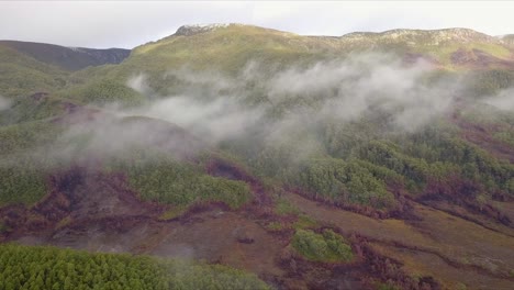 Aerial-flight-over-foggy-mountains-and-green-and-red-forest-in-Tasmania-in-Australia,-long-shot-moving-forward