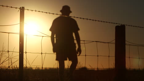 Silhouette-of-farmer-walking-along-and-away-from-wire-fence