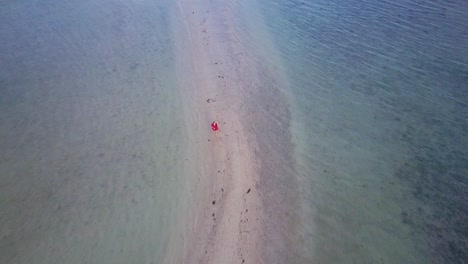Aerial-view-of-young-brunette-woman-in-red-dress-walking-on-sandbar-in-Asia---camera-tracking-backwards-and-pedestal-up