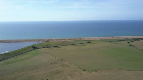 Wide-aerial-tracking-forward-over-a-field-at-the-west-side-of-Chesil-Beach,-Dorset