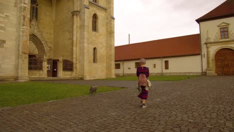 Following-shot-of-girl-with-backpack-and-short-hair-in-front-of-orthodox-church-in-Alba-Iulia,the-citadel-alba-carolina