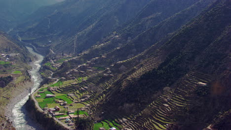 A-picturesque-village-with-beautiful-scenes-of-mountains-and-river-aerial-view,-as-well-as-charmingly-crafted-greenery-with-a-road-where-traffic-is-moving