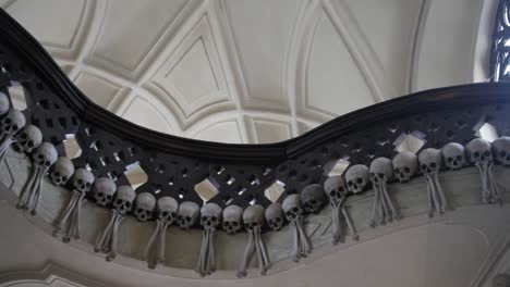 Panning-shot-across-terrifying-stair-banister-railing-decorated-with-human-remains-skull---bones-in-Sedlec-Ossuary-Roman-Catholic-Chapel,-Czech-Republic
