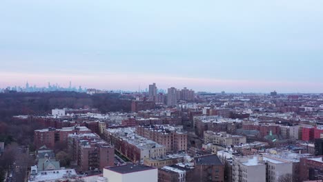 Drone-rise-over-central-Brooklyn,-New-York,-just-before-sunset,-revealing-the-Manhattan-skyline-in-the-distance