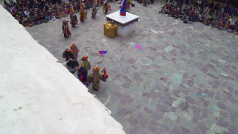 Monks-with-colorful-dresses-dancing-in-front-of-tourists-at-Hemis-festival-in-monastery,-shot-from-roof-above,-dolly-shot