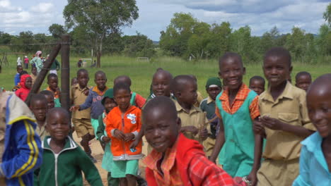 Afrikanische-Kinder-Lächeln-Und-Winken-In-Die-Kamera,-Während-Sie-Vor-Ihrer-Grundschule-Im-Ländlichen-Simbabwe-Stehen,-Zeitlupen-Steadycam-Bewegung