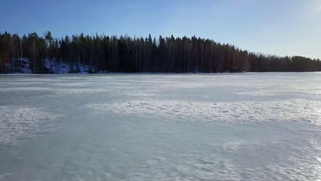 Aerial-sideways-low,-sunshine-reflected-on-frozen-winter-ice-lake