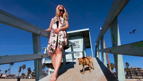 Beautiful-young-blonde-girl-and-cute-dog-walk-down-a-sandy-ramp-on-Venice-Beach