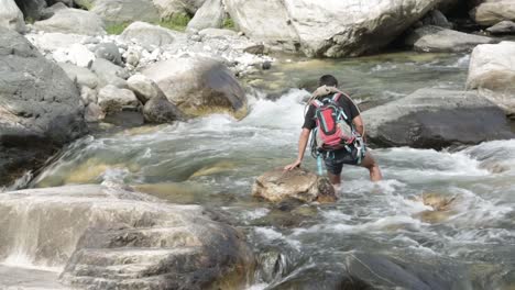 A-trainer-crossing-the-flowing-mountainous-river-in-the-upper-Himalayas,-Uttarakhand,-India