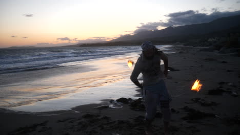 Un-Bailarín-De-Arte-De-Flujo-Masculino-En-Silueta-Interpretando-Su-Fuego-Girando-En-La-Playa-Al-Atardecer-Con-Olas-Oceánicas-En-Cámara-Lenta