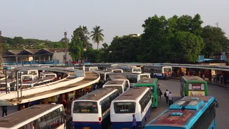 Vista-Aérea-De-La-Pila-De-Autobuses-Que-Ingresan-A-La-Estación-De-Autobuses-Y-Los-Pasajeros-Ocupados-En-Conseguir-Los-Autobuses-En-La-Majestuosa-Estación-De-Autobuses-De-Bengaluru,-India