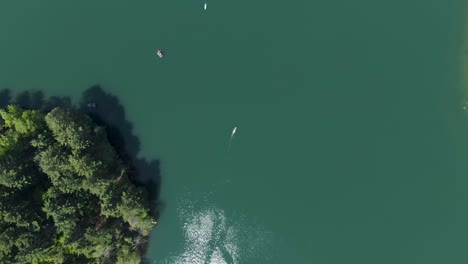 Toma-Aérea-Sobre-Kayaks-De-Movimiento-Lento-En-Un-Lago-Verde-Durante-Una-Calurosa-Y-Soleada-Tarde-De-Verano