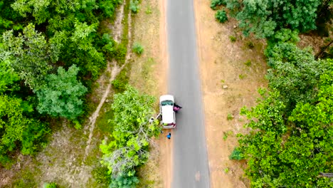 Aerial-view-of-people-running-along-the-asphalt-road-between-a-forest-and-car-stop-in-road