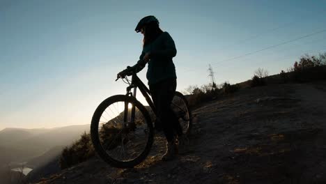 Mädchen-Schiebt-Bei-Sonnenuntergang-Ihr-Fahrrad-Auf-Den-Gipfel-Eines-Berges