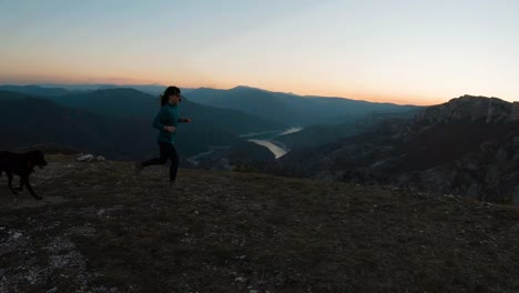 Young-girl-running-with-a-labradot-dog-on-a-mountain-at-sunset-during-autumn