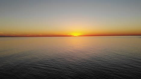 Filmische-Luftdrohne,-Die-Sich-Langsam-Dem-Wasser-Nähert-Und-Einen-Wunderschönen-Sonnenuntergang-über-Dem-Meer-überblickt