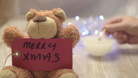 Cute-teddy-bear-with-Merry-Christmas-greeting,-candles-and-background-lights