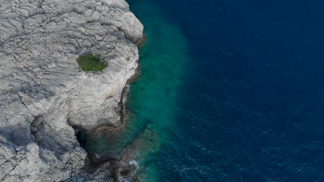 AERIAL:-Drone-looking-down-to-rocky-coastline-next-to-turquoise-sea