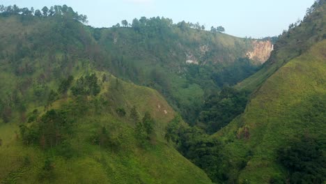 Sunny-approach-drone-shot-of-cliffs,-jungle,-and-Sipiso-Piso-waterfall-in-North-Sumatra,-Indonesia