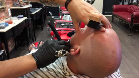 Adult-Male-at-a-retro-style-barbershop-having-his-facial-hair-shaved-off-by-a-professional-barber-using-a-clipper-machine-gloves-customer