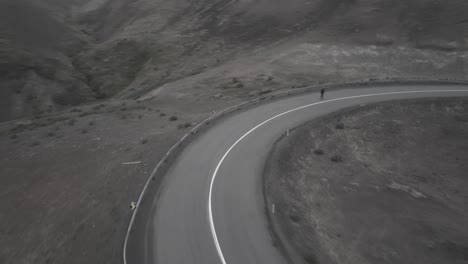 Drone-shots-of-skater-going-downhil-on-curvy-road-in-a-foggy,-dramatic-landscape-in-Iceland
