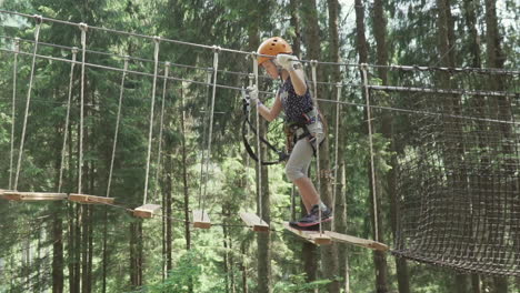 Little-girl-with-red-hair-crosses-a-tibetan-bridge-in-adventure-park-in-the-Italian-Alps,-slow-motion