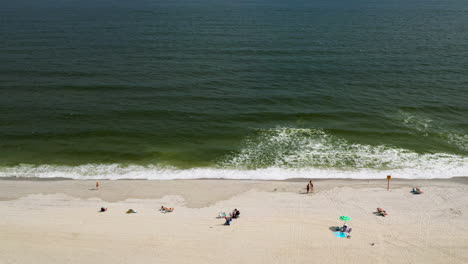 Aerial-drone-shot-pan-left-facing-the-ocean-looking-at-the-shoreline-and-the-different-people-on-the-beach