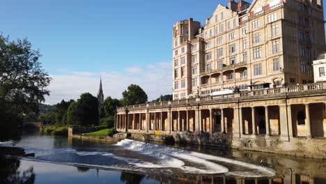 Toma-Estática-En-Cámara-Lenta-De-Pulteney-Weir-Y-El-Hotel-Empire-En-Bath,-Somerset-En-La-Hermosa-Mañana-De-Verano-Con-Cielo-Azul-Y-Luz-Dorada