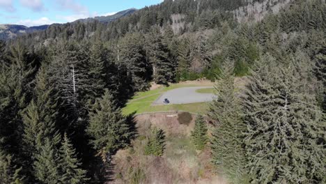 Drone-flies-towards-parking-lot-in-the-midst-of-pine-trees-on-the-coast