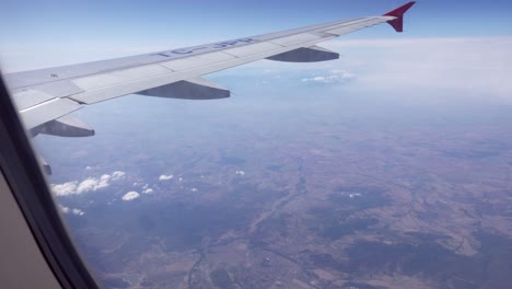 View-of-an-airplane-wing-as-it-flies-high-above-the-mountain-terrain-below