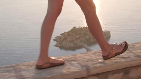 Schöne-Dame,-Die-Auf-Einem-Aussichtspunkt-Mit-Blick-über-Die-Küste-Montenegros-über-Sveti-Stefan-Während-Eines-Wunderschönen-Sonnenuntergangs-Spazieren-Geht