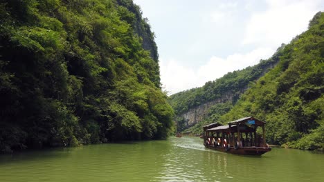 Zhangjiajie,-China---August-2019-:-Traditional-wooden-boats-sailing-on-the-waters-of-a-small-narrow-lake-between-tall-and-high-rocky-cliffs-of-the-majestic-Grand-Canyon-in-Zhangjiajie-National-Park