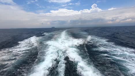 View-from-back-of-boat-watching-the-water-wake-from-engines-power-through-deep-blue-ocean-sea-in-Thailand