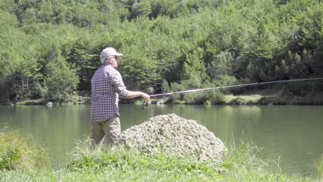 Man-fishing-ion-a-mountain-lake,-medium-shot-4K
