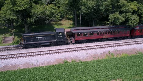 Una-Vista-Aérea-De-Una-Locomotora-Diésel-Tirando-De-Coches-De-Pasajeros-Antiguos-A-Través-De-La-Campiña-Amish