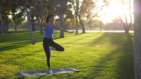 A-beautiful-young-woman-yogi-almost-falling-over-and-losing-balance-in-a-one-legged-prayer-hands-yoga-pose-on-a-mat-in-the-park-at-sunrise