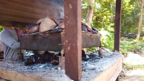 Imágenes-De-Un-Hombre-Cocinando-Bajo-Fuego-Con-El-Uso-De-Cáscaras-De-Coco-A-Lo-Largo-De-La-Calle-Con-El-Pequeño-Techo-Encima-Del-Fuego-Y-Una-Dama-En-El-Fondo