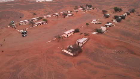 Luftaufnahme-Mit-Drohne-über-Touristen-In-Einem-Verlassenen,-Mit-Sand-Bedeckten-Dorf-In-Der-Wüste-Von-Dubai,-Vereinigte-Arabische-Emirate