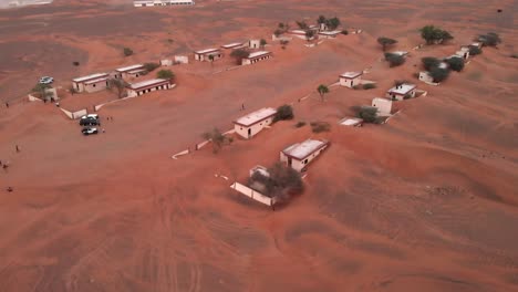 Vista-Aérea-Con-Drones-Sobre-Turistas-En-Un-Pueblo-Abandonado-Cubierto-De-Arena-En-El-Desierto-De-Dubai,-Emiratos-árabes-Unidos