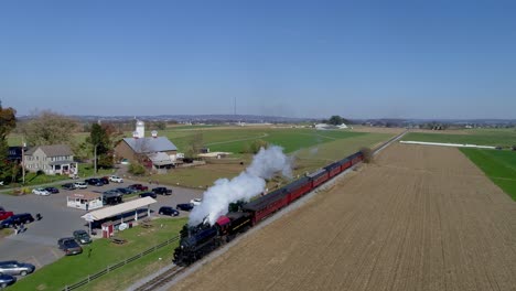 Luftaufnahme-Einer-Antiken-Restaurierten-Dampflokomotive-Mit-Personenwagen,-Die-Durch-Die-Landschaft-Fährt-Und-Dabei-Schwarzen-Und-Weißen-Rauch-Und-Dampf-Bläst