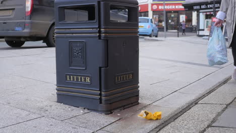 Person-walking-passed-a-trash-bin-ignoring-litter-outside-thrown-incorrectly,-wide-pan-shot