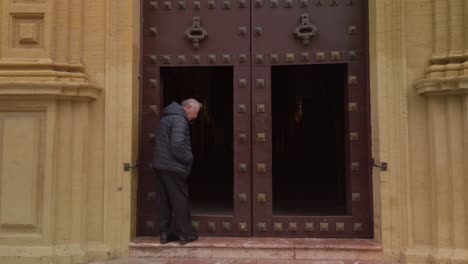 Spanish-senior-man-stands-in-doorway-of-historic-church-and-walks-away
