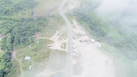 Aerial-view-of-rural-single-track-road-on-green-hills,-seen-from-above-fog-and-clouds-on-wet-season