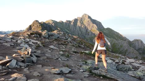 A-young-woman-with-long-brown-hair-is-walking-alone-over-rocks-and-stones-on-top-of-mountain-Festvågtind-in-Lofoten-during-the-midnight-sun