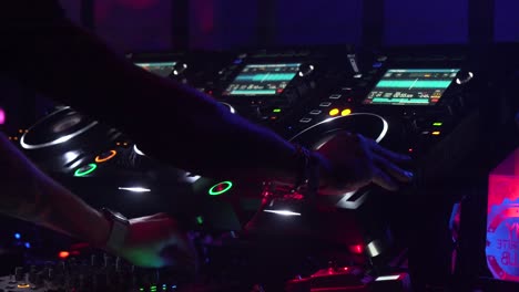 Close-shot-of-DJ-mixing-table-with-the-hand-of-a-DJ-mixing-in-a-dance-club