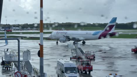 Flugzeugaktivität-Auf-Dem-Flughafenvorfeld-Durch-Ein-Mit-Regentropfen-Bedecktes-Fenster