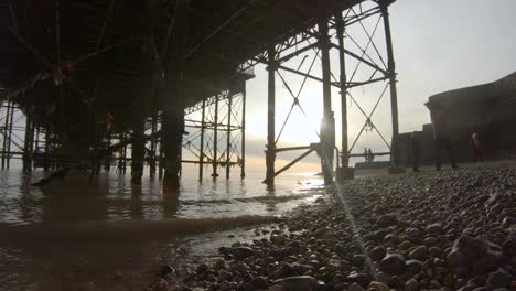 Brighton-Pier-seen-from-underneath,-framework,-sunset-and-sun-flare-with-people-walking-around